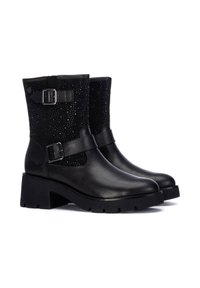 Botas de tobillo negras con una puntera de cuero suave y un empeine de tela texturizada y con tachuelas. Presentan una correa con hebilla y un tacón de goma grueso.