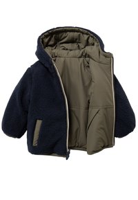 Marineblauwe fleecejas met capuchon, beige voering, ritssluiting aan de voorkant en zijzak. Zachte textuur met pofmouwen en een oversized pasvorm.