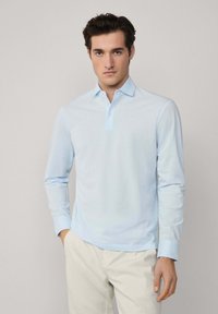 Svijetloplava dugosveđa polo majica s gumbom na ovratniku, izrađena od mekanog materijala. Sadrži suptilnu teksturu i dizajn slim fit.