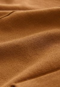 Țesătură maro tricotată, cu o suprafață netedă și texturată. Model de nervuri vizibile, evidențiind variații în grosime și adâncimea culorii.