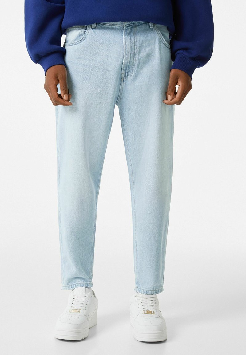 Ljust blå denimjeans med tapered fit, som har fem fickor och en urtvättad yta, kombinerat med vita sneakers och en blå sweatshirt.