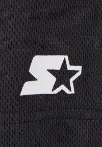 Crni mrežasti materijal s bijelim logotipom koji sadrži apstraktnu formu i element zvijezde; vidljive detalje šivanja duž ruba.