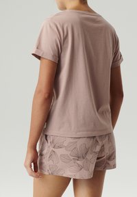 Jasnoróżowa koszulka z krótkim rękawem z podwiniętymi mankietami, w zestawie z dopasowanymi szortami z ciemnymi kwiatowymi wzorami, wykonana z miękkiego materiału.