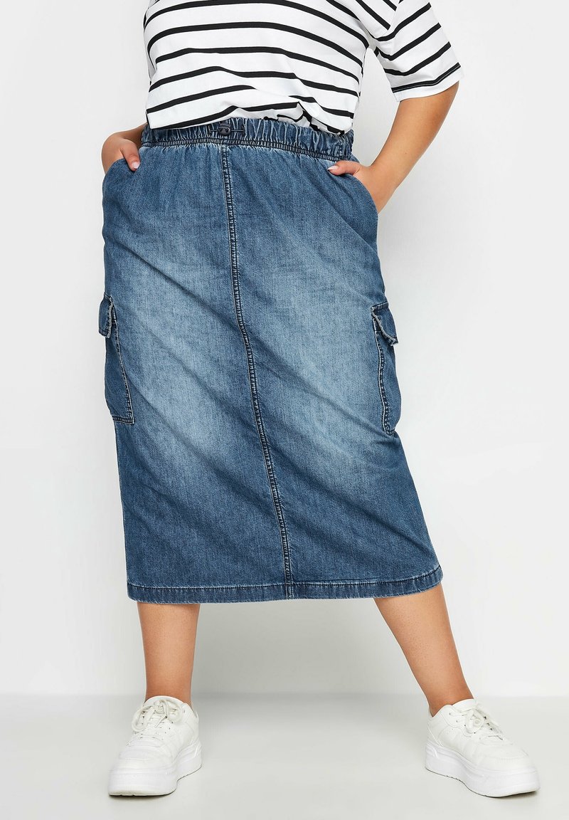 Falda midi de mezclilla con cintura elástica, bolsillos laterales y costuras visibles. Color azul claro con una textura suave. Combinada con una camiseta a rayas.