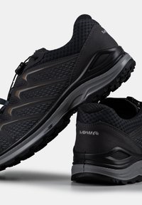 Zwarte atletische schoenen met een bovenwerk van textuurmesh en grijze accenten. Beschikt over een gevoerde zool, een uitgesproken looppatroon en een elastisch vetersysteem.