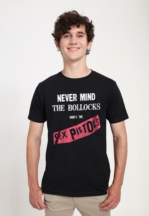 Ung mand med krøllet hår, som smiler og bærer en sort T-shirt med hvid og rød tekst, der refererer til bandet Sex Pistols.
