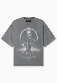 Pelēka kokvilnas T-krekls ar vaļīgu piegriezumu, uz kura ir grafiskais attēls ar statuju, kas paceļas uz augšu, apvienota ar apļveida gaismu un putniem.