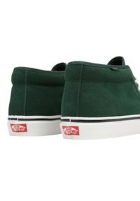 Scarpe alte in suede verde con lace bianchi, suola in gomma, dettagli neri e logo rosso sul tallone. Texture liscia e dettagli cuciti.