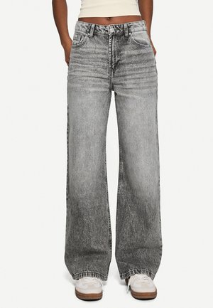 Wide-legged jeans in faded gray denim, featuring a high waist, front pockets, and subtle whiskering details. Paired with white sneakers.