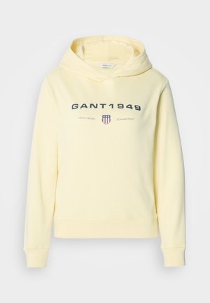 Dzeltena kapuces džemperis no mīksta auduma ar drukātu logotipu "GANT 1949" un aizsarga grafiku krūtīs. Garas piedurknes, riboti aproces.