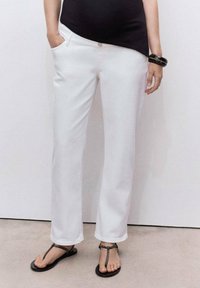 Pantaloni bianchi a gamba dritta in cotone con due tasche laterali. Abbinati a sandali neri piatti con una fascia decorativa.