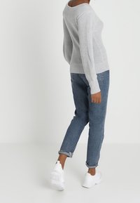 Šedý pletený svetr s širokým výstřihem, zkombinovaný s modrými džínami s manžetami a bílými teniskami, vystihující uvolněný střih a žebrovanou texturu.