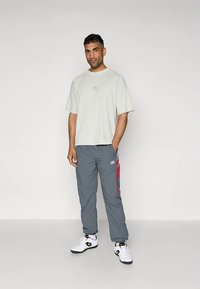 Világosszürke, túlméretezett póló és szürke melegítőnadrág piros részletekkel. Fehér sportcipő fekete díszítéssel. Egyszerű, laza szabás.