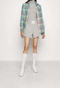 Rutig skjorta i teal, gult och röd över en grå polotröja och matchande shorts. Vita knästrumpor och sneakers fulländar looken.