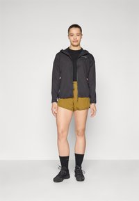 Black lightweight jacket with a hood, paired with olive green shorts. The outfit includes black socks and hiking shoes.