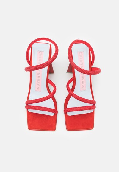 Κόκκινες σουέτ ψηλοτάκουνες σανδάλι με τετράγωνη μύτη, που διαθέτουν περιστρεφόμενες υφασμάτινες λωρίδες και συμπαγές τακούνι. Λευκή σόλα με λογότυπο.