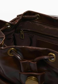 Pruun nahk kott sisestruktuur kuldse viimistlusega riistadega, nööriga sulgemine, lukuga tasku ja sileda kangaga vooder, mis võimaldab mugavat juurdepääsu ja ladustamist.