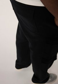 Schwarze Cargo-Hosen mit Seitentaschen, aus einem strukturierten Stoff gefertigt. Verfügt über eine lockere Passform und verstärkte Nähte für Langlebigkeit.