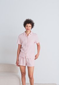 Ljusrosa kortärmade pyjamas i texturerad tyg, med en knäppning på skjortan och ett bröstfack samt matchande shorts.