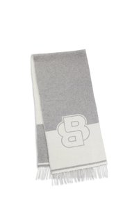 Écharpe en laine grise et blanche, présentant un motif géométrique avec un logo surdimensionné, et terminée par des bords à franges.