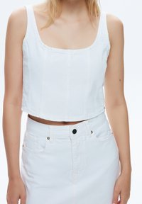 Top corto blanco de mezclilla con escote cuadrado y superficie texturizada, combinado con una falda de mezclilla blanca con cierre de botón.