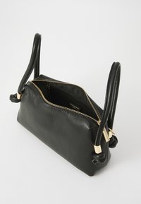 Sac à main en cuir noir avec des poignées nouées doubles, une fermeture éclair dorée et une texture lisse. Le dessus ouvert révèle un intérieur spacieux.