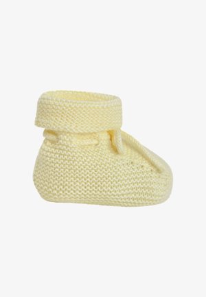 Chausson bébé jaune doux en tricot avec bord replié et détail de lien latéral sur fond blanc.