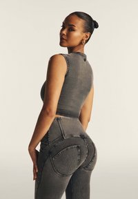 Una modella in un crop top in denim grigio aderente e jeans a vita alta con tasche posteriori curve uniche, che mostrano una texture liscia.