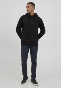 Felpa nera in cotone con tasca frontale e cappuccio con cordino, abbinata a pantaloni slim-fit blu navy e sneakers nere con suola bianca.