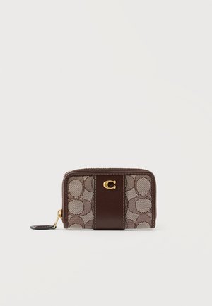 Καφέ πορτοφόλι με φερμουάρ γύρω-γύρω, με χαρακτηριστικό κυκλικό μοτίβο, σκουρό καφέ δερμάτινη κεντρική λωρίδα και χρυσό μεταλλικό λογότυπο "C" στο μπροστινό μέρος.