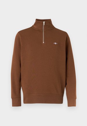 Brown pullover sweater with high collar and half zip. Made of soft fabric, featuring ribbed cuffs and a small logo on the chest.