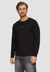 Zwarte lange mouwen t-shirt van katoen met een ronde halslijn en een klein logo op de borst. Draagt met grijze jeans.