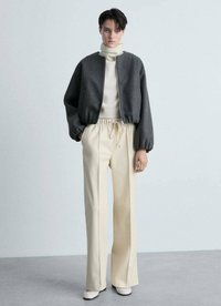 Giacca bomber grigia cropped con polsini elasticizzati, dolcevita crema e pantaloni crema a vita alta. Tessuto morbido e vestibilità rilassata.