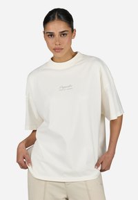 Oversized cream t-shirt made from soft cotton, featuring a round neck and embroidered logo on the chest. Short, wide sleeves.