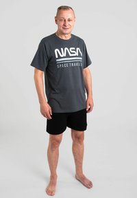 T-shirt in cotone grigio con il logo "NASA" e la scritta "SPACE TRAVEL". Indossato con pantaloni corti neri. Design semplice, maniche corte e vestibilità comoda.