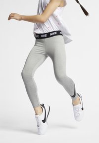 Gray leggings with a black Nike waistband and black side accents, paired with white sneakers with a black swoosh. Performative fit, stretchy fabric.