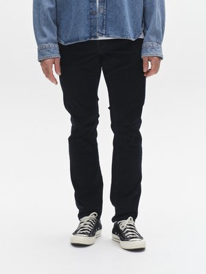 Traper jakna svijetloplave boje s kopčanjem na gumbe, uparena s crnim uskim trapericama. Crne tenisice s bijelim vezicama i gumenim potplatima.