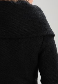 Black textured coat featuring a wide collar and a tailored fit, with a soft fabric that adds depth to the design.