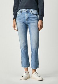 Jasnoniebieskie dżinsy z krojem 7/8 i rozszerzanymi nogawkami. Posiadają średni stan, kontrastowe szwy oraz delikatne przetarcia. W zestawie z białymi trampkami.