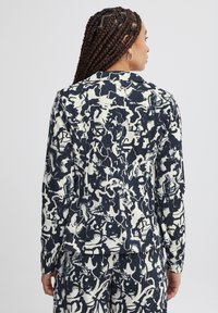 Patterned blazer featuring a navy and cream abstract design, with long sleeves and a smooth fabric finish. Visible stitching details at seams.