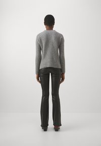 Maglione grigio a costine con maniche lunghe, abbinato a pantaloni aderenti in pelle nera. L'outfit presenta un design semplice ed elegante.