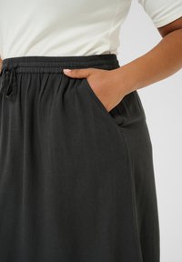 Čierna, voľná sukňa s elastickým pásom a šnúrkou na sťahovanie. Obsahuje bočné vrecká a mäkkú, textúrovanú látku.
