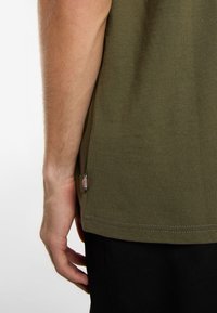 T-shirt verde oliva con etichetta laterale, texture a coste e orlo dritto, dotato di maniche corte e vestibilità rilassata.