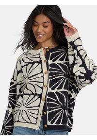 Cardigan bleu marine et crème avec de grands motifs floraux, tissu tricot léger et boutons en bois sur le devant. Coupe décontractée avec des poignets côtelés.