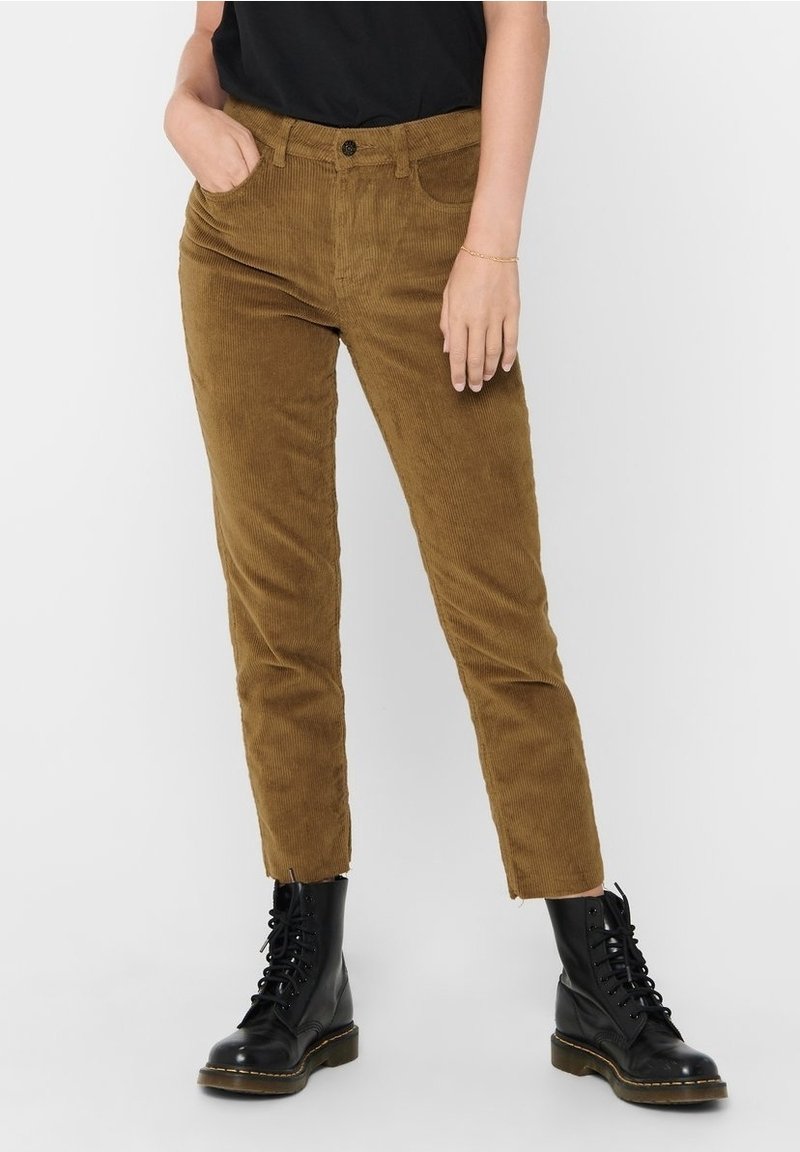 Pantalon en velours côtelé marron à coupe ajustée, avec poches avant et fermeture par bouton à la taille, assorti à des bottes noires à lacets.