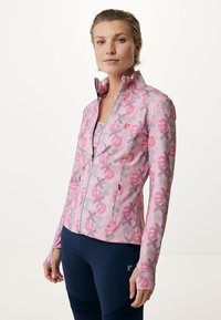 Giacca leggera con zip di colore rosa, decorata con un motivo grafico di simboli. Presenta maniche lunghe e un colletto alto, realizzata in tessuto elasticizzato.