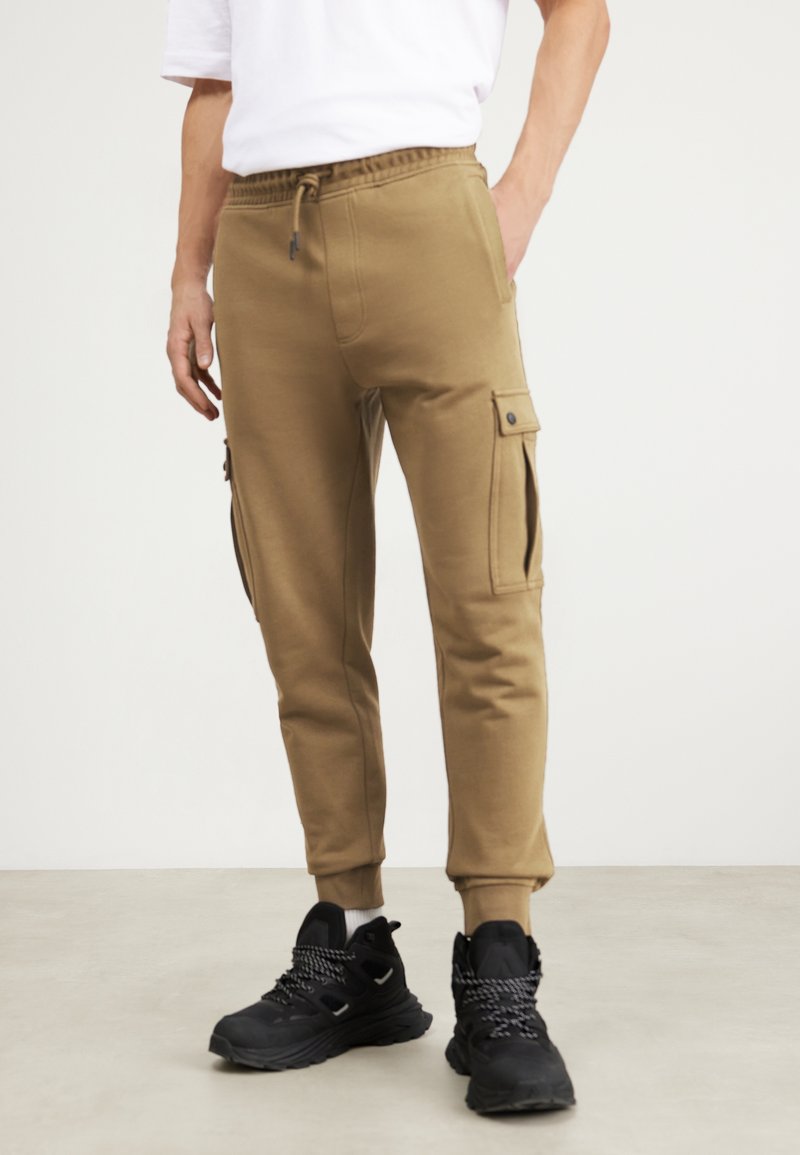 Kaki joggerbyxor med elastisk midja, sidofickor och ribbade ankle cuffs. Stylar med svarta sneakers och en vit t-shirt.