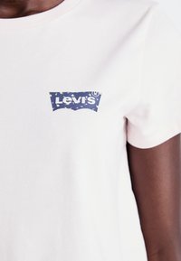T-shirt rose pâle à manches courtes en coton, avec un logo bleu Levi's orné d'un motif abstrait coloré sur la zone de la poitrine.