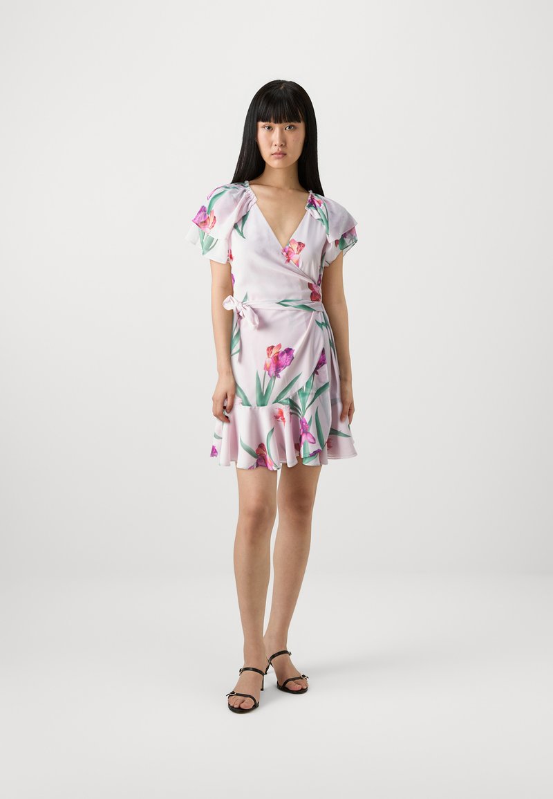 Robe portefeuille florale en tissu rose clair avec des manches courtes à volants, décolleté en V profond et ceinture à la taille accentuée ; présente des motifs violets et verts.