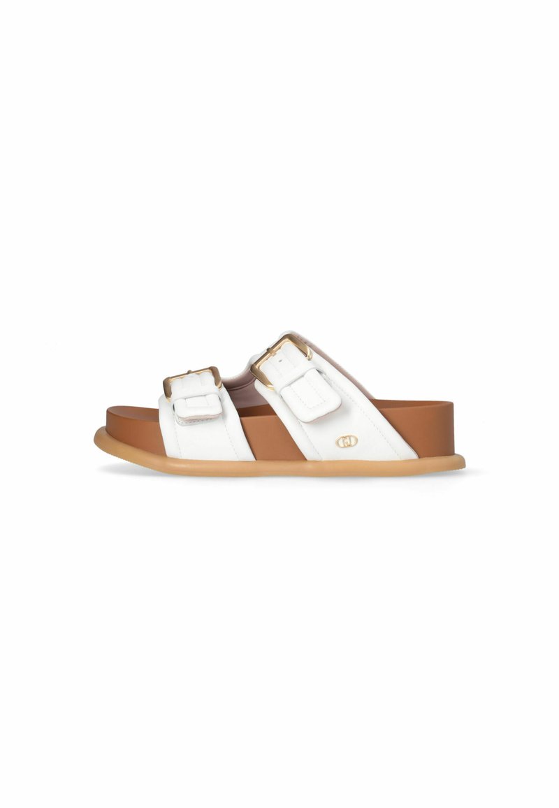 Sandales plates blanches avec deux brides ajustables, boucles dorées et semelle en caoutchouc beige, présentant une texture lisse et un accent de marque discret.